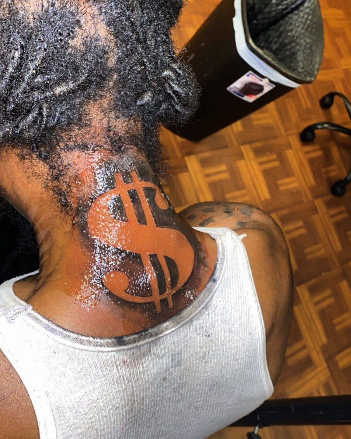 Dollar sign negative shading tattoo on the back of a person's neck