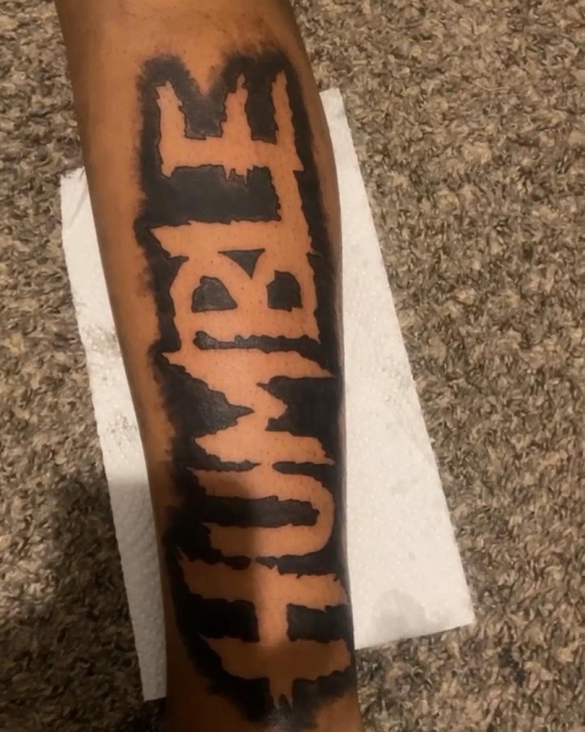 Forearm tattoo of the word HUMBLE created using negative space and black ink.