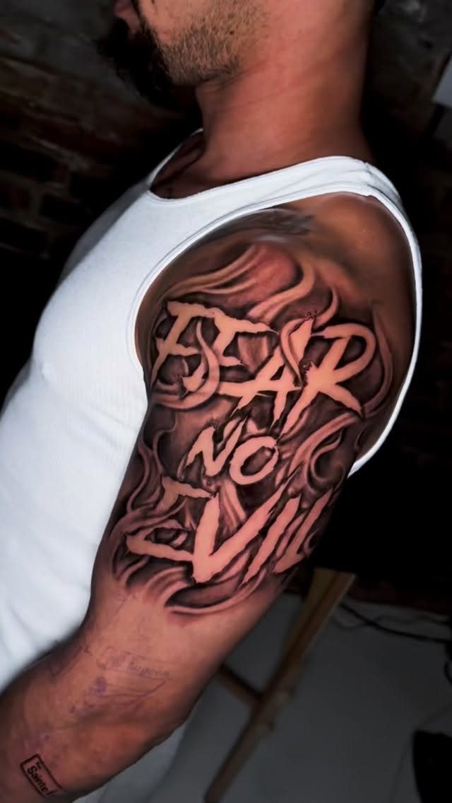 Negative space tattoo on a man's arm reading FEAR NO EVIL with smoke patterns