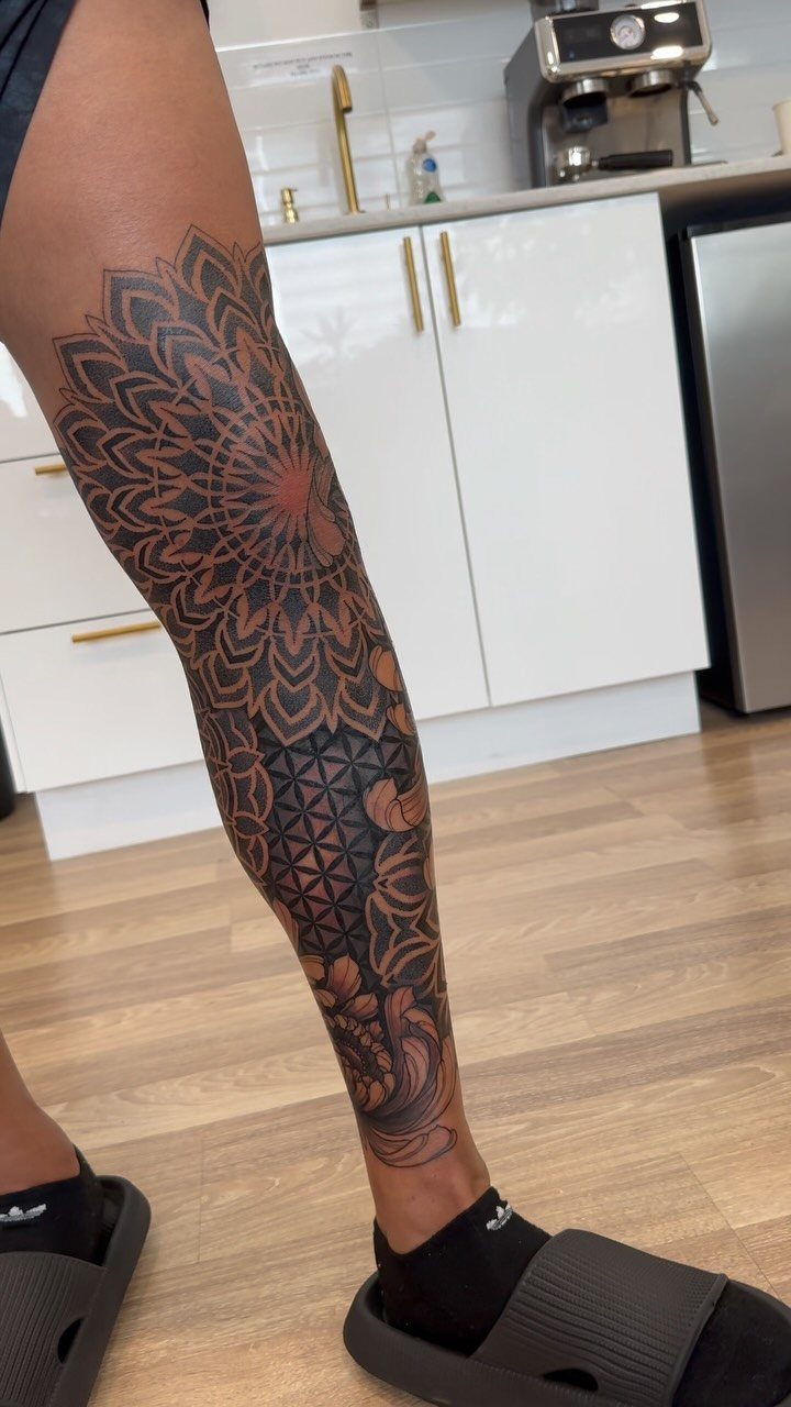 Intricate black ink mandala and geometric tattoo covering a person's lower leg