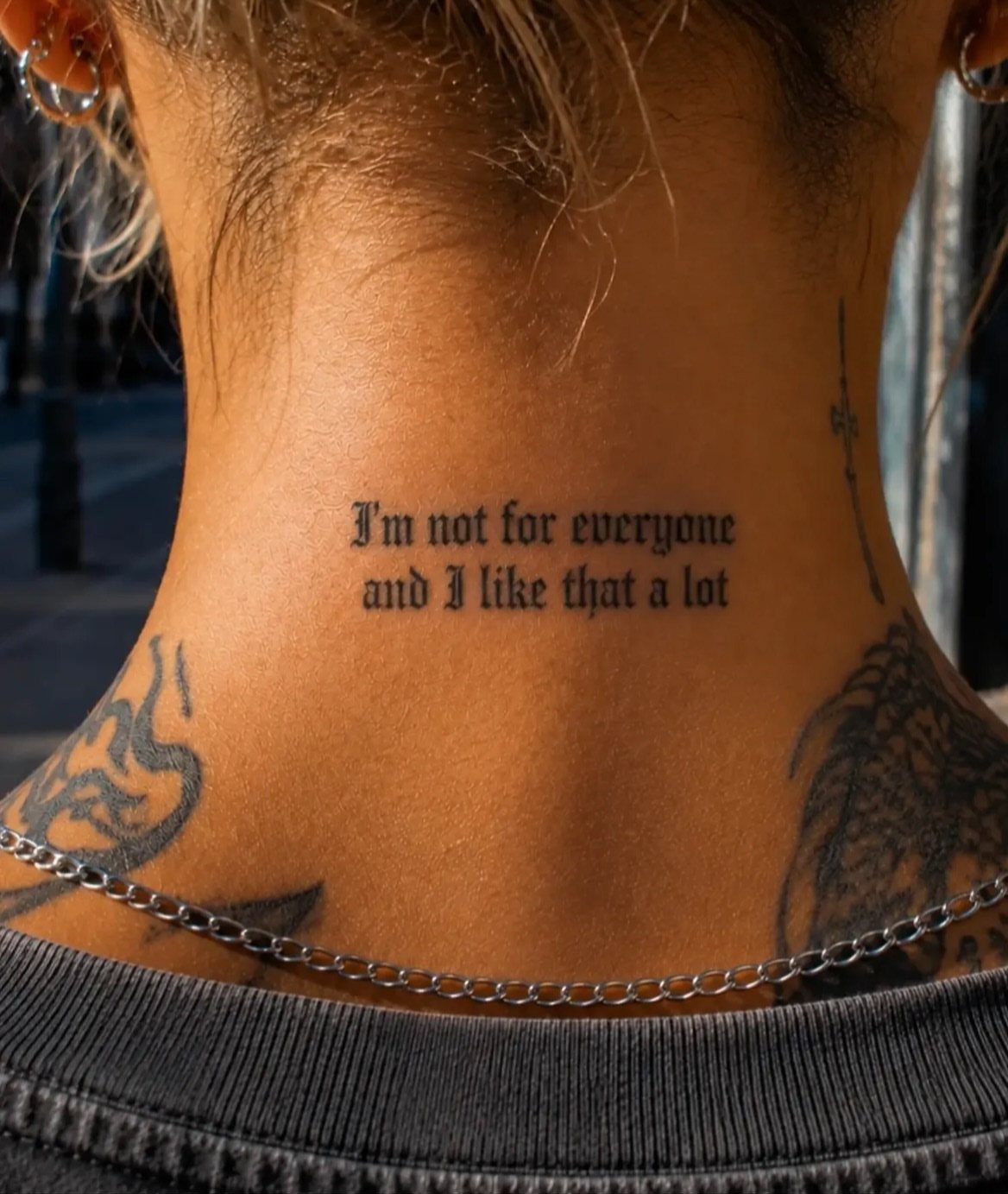 Black ink quote tattoo on the back of a neck in gothic lettering.