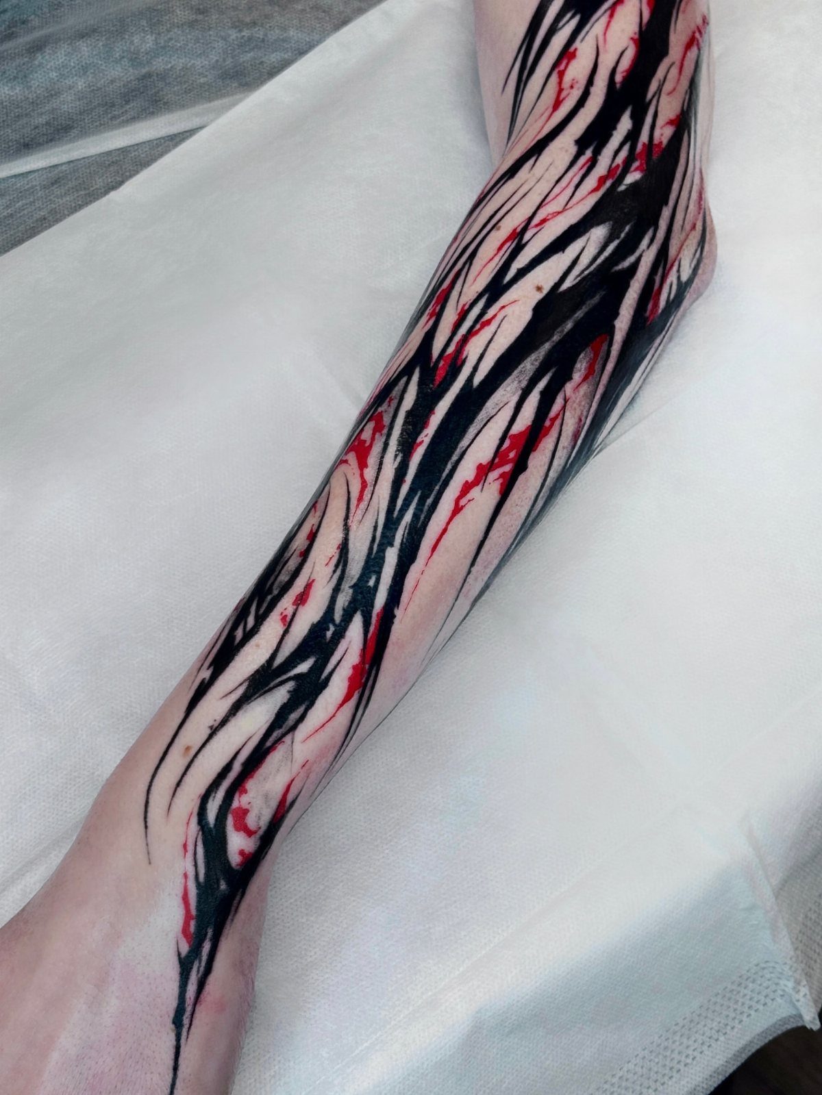 Forearm tattoo with bold black abstract strokes and thin red accent lines.