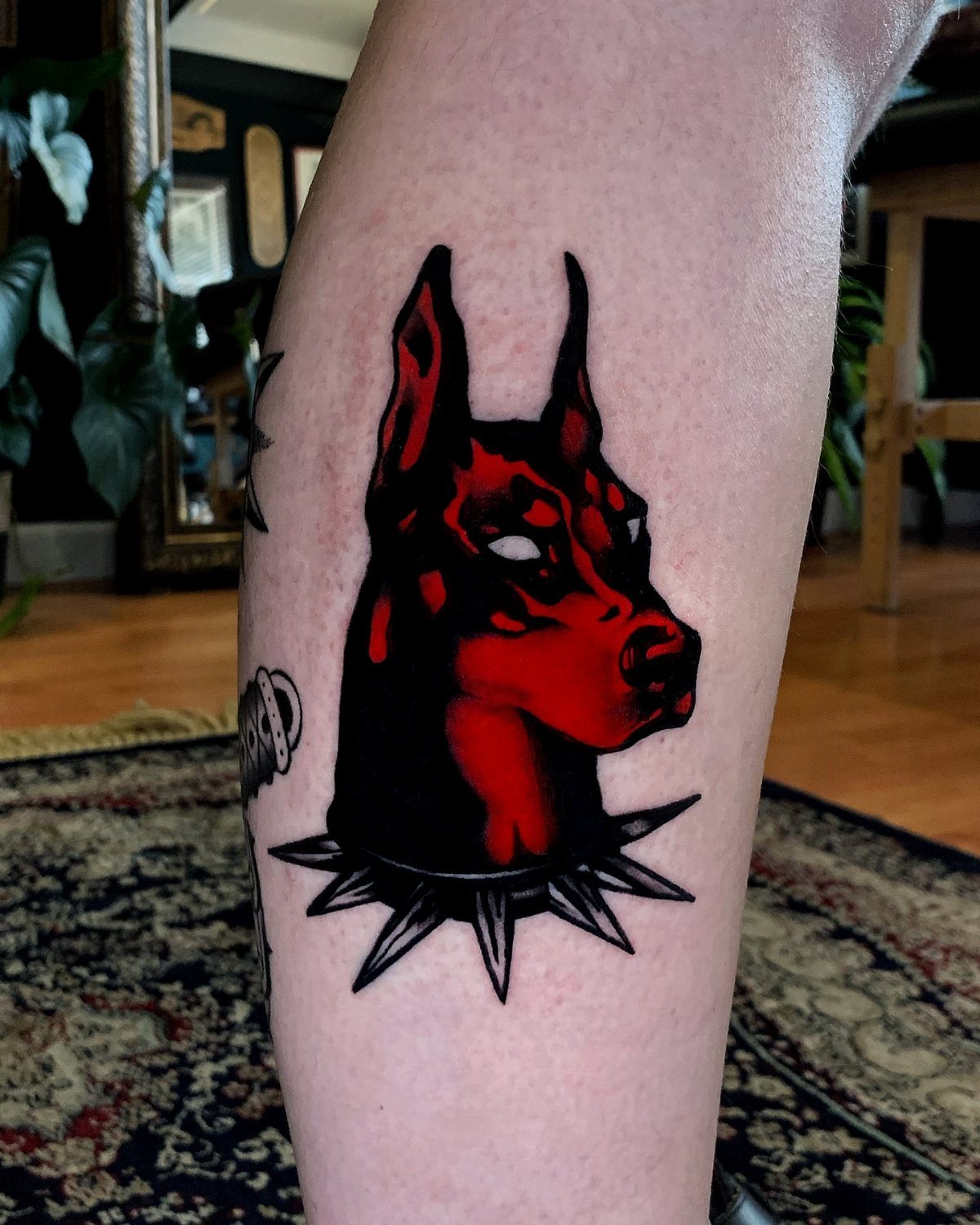 Doberman dog tattoo in red and black ink on a person's leg