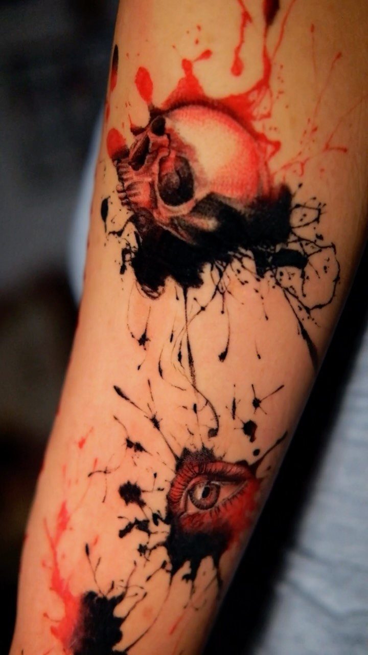 Skull and eye tattoo in red and black splatter style on an arm.