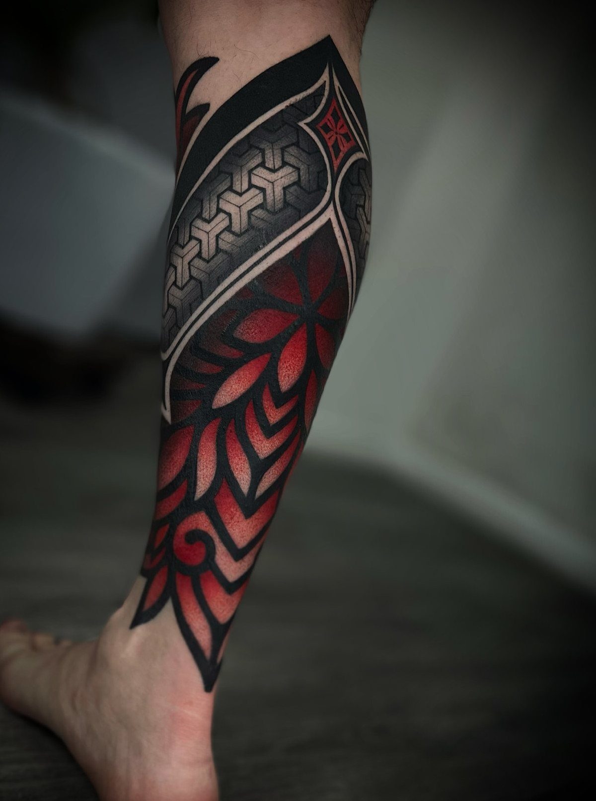 Leg tattoo with red and black geometric patterns and stylized floral elements.