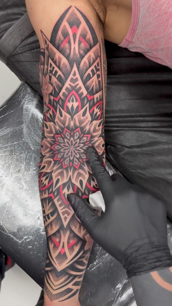Symmetrical mandala tattoo in red and black ink on a person's forearm