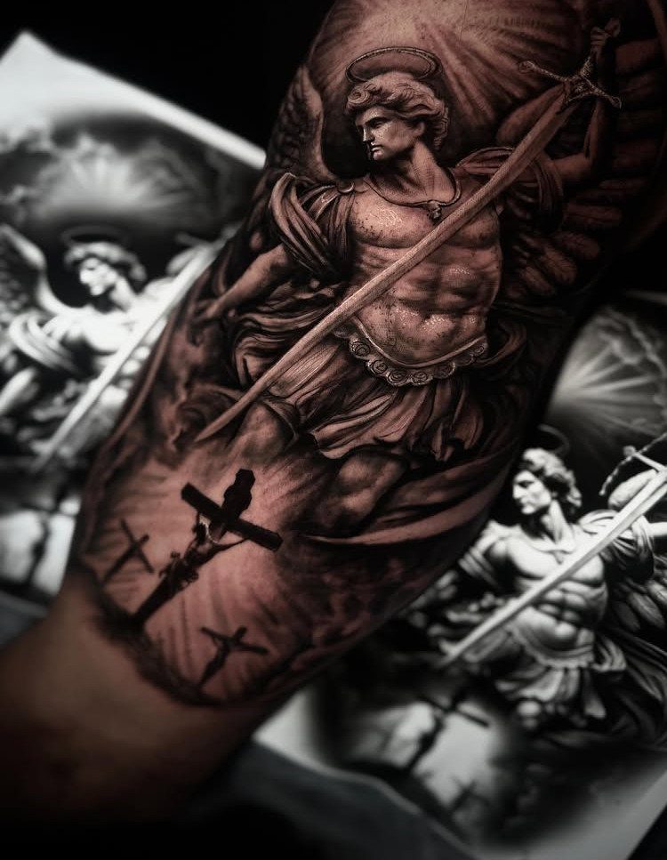 Archangel tattoo with wings and sword on a forearm with three crosses below.