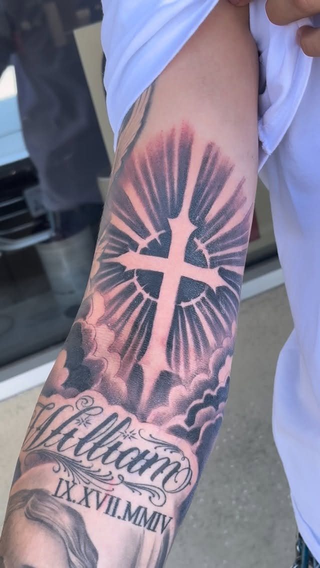 Cross tattoo with radiating light beams and clouds on a person's forearm