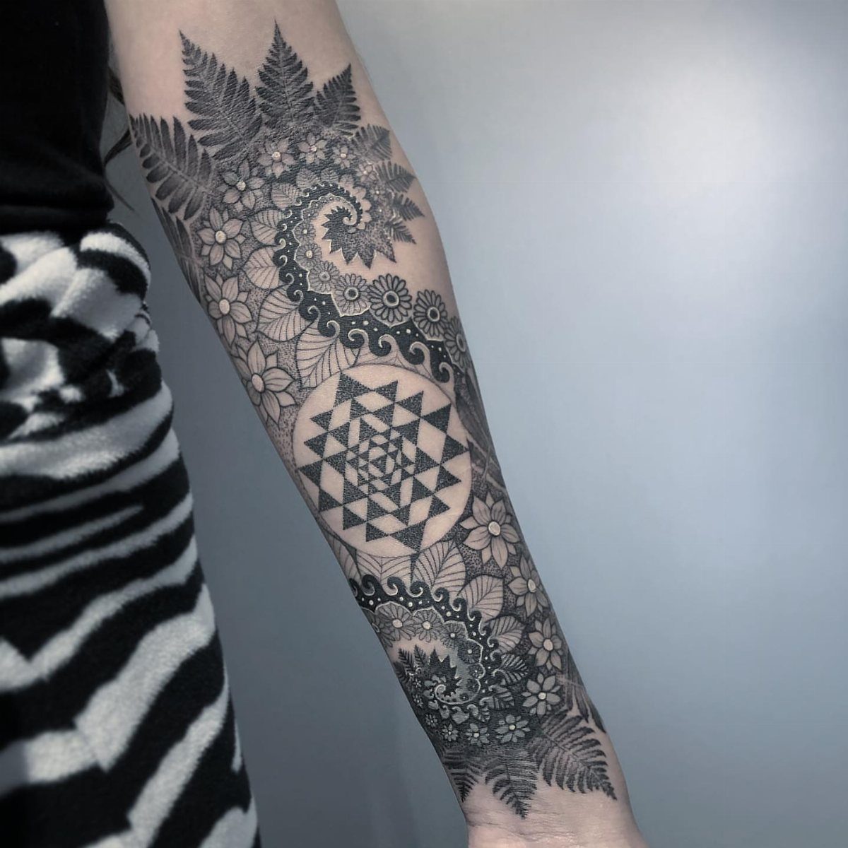 Sacred geometry tattoo on a forearm with intricate floral and fern patterns.