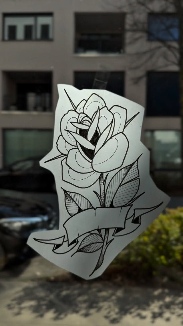 Single rose tattoo stencil with a ribbon banner on translucent paper.