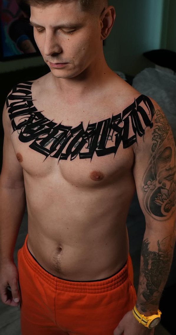 Man with black calligraphic chest tattoo and a detailed arm sleeve tattoo.