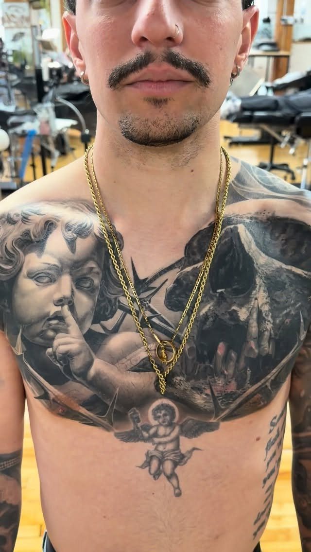 Man with a large black and grey chest tattoo of a cherub and skull.