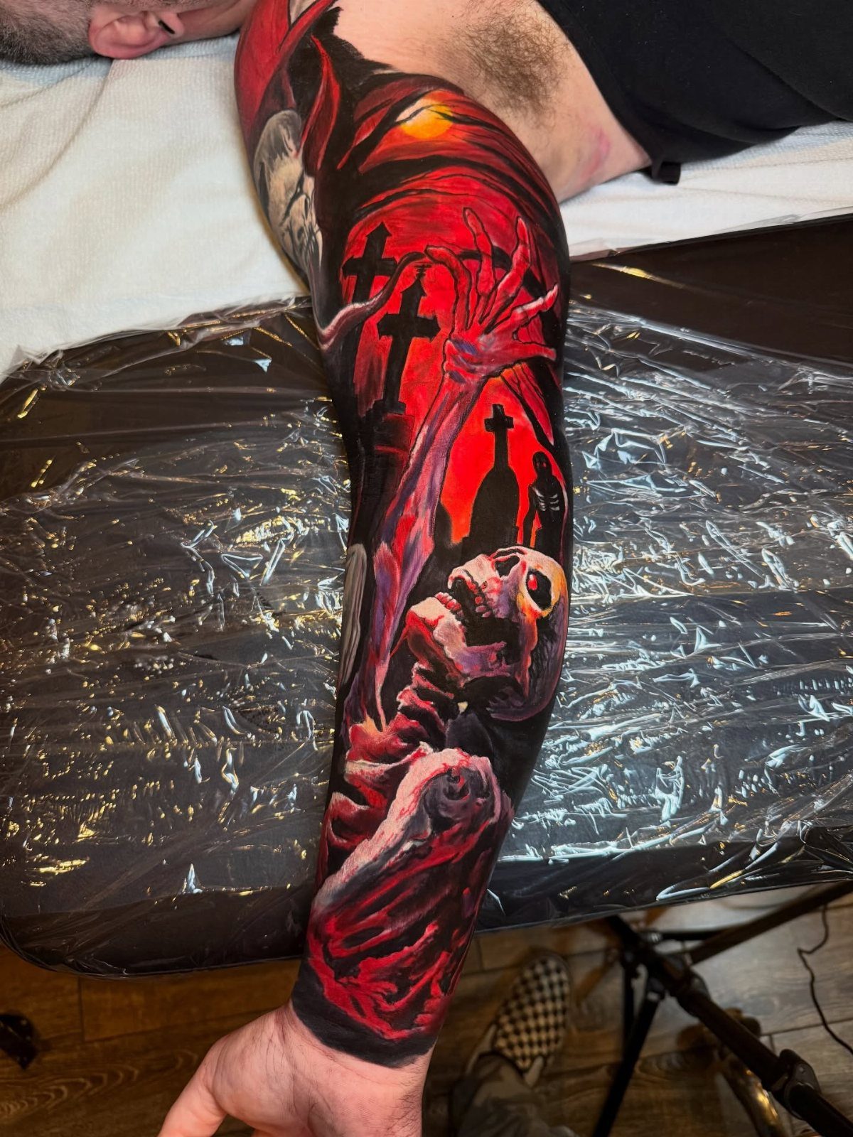Full sleeve tattoo with a skull and crosses in dark red and black ink.