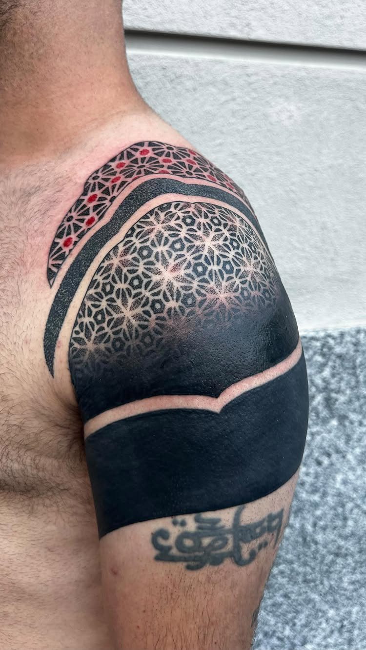 Geometric shoulder tattoo with black patterns and red accents covering an old tattoo.