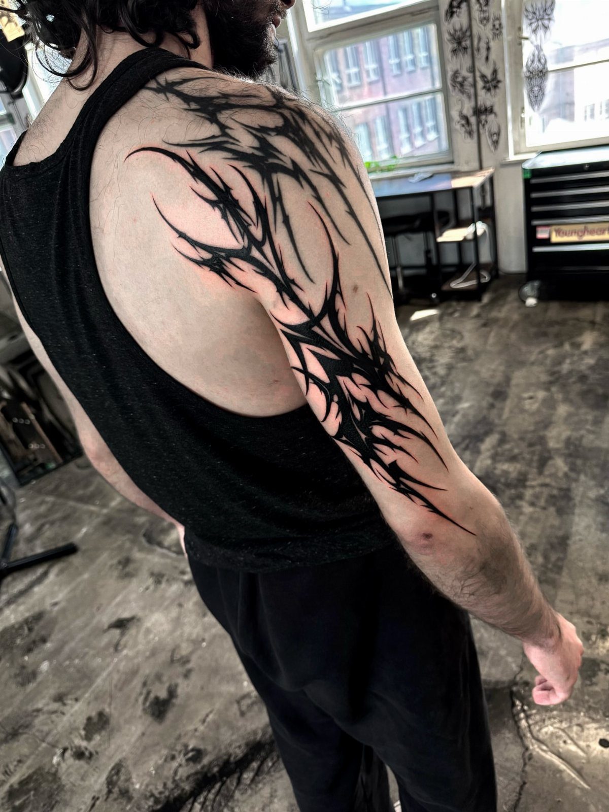 Black ink shoulder tattoo with sharp organic shapes and negative space gaps.