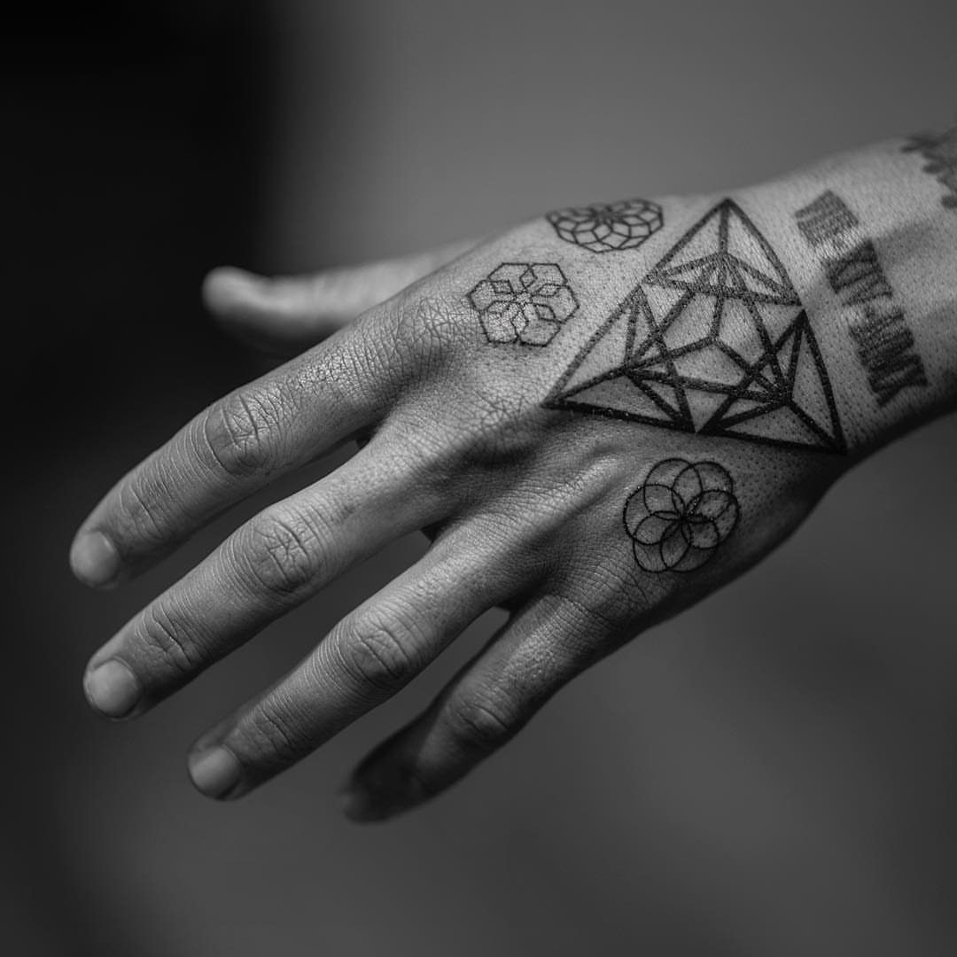 Hand with geometric single needle tattoos including a large triangle and hexagonal patterns.