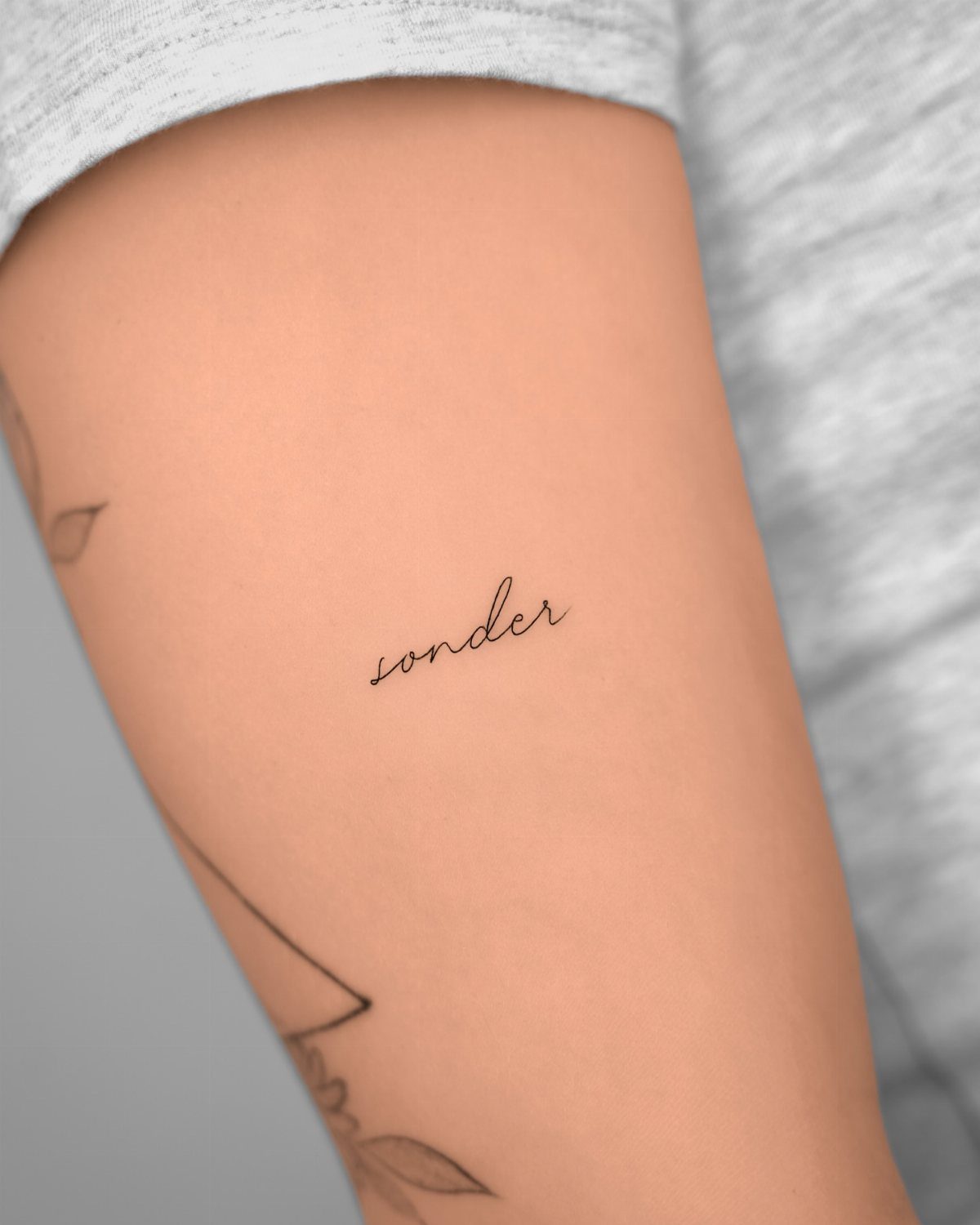 Small cursive tattoo of the word sonder on a person's upper arm.