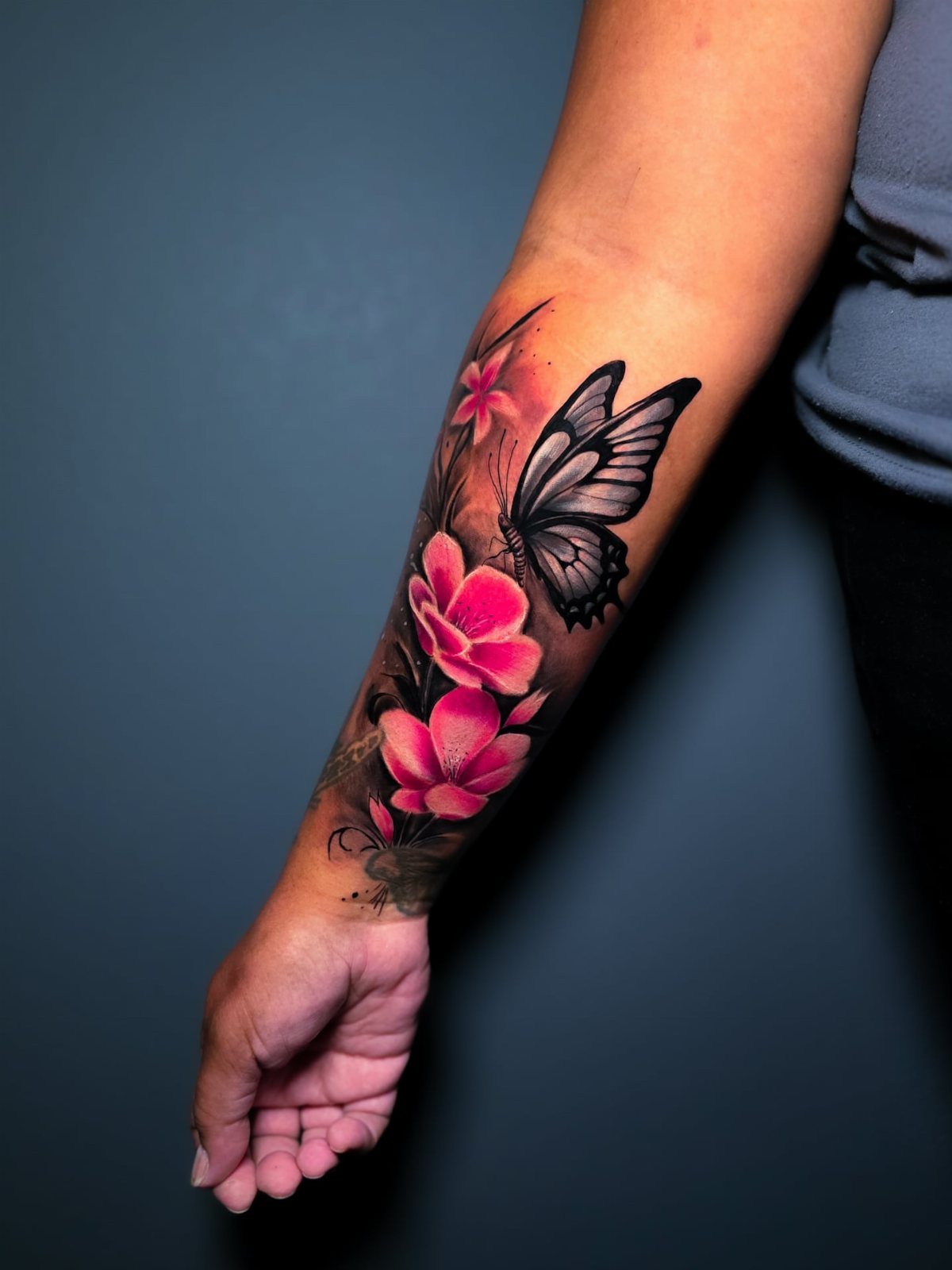 Tattoo of a black butterfly and pink flowers on a dark skin forearm