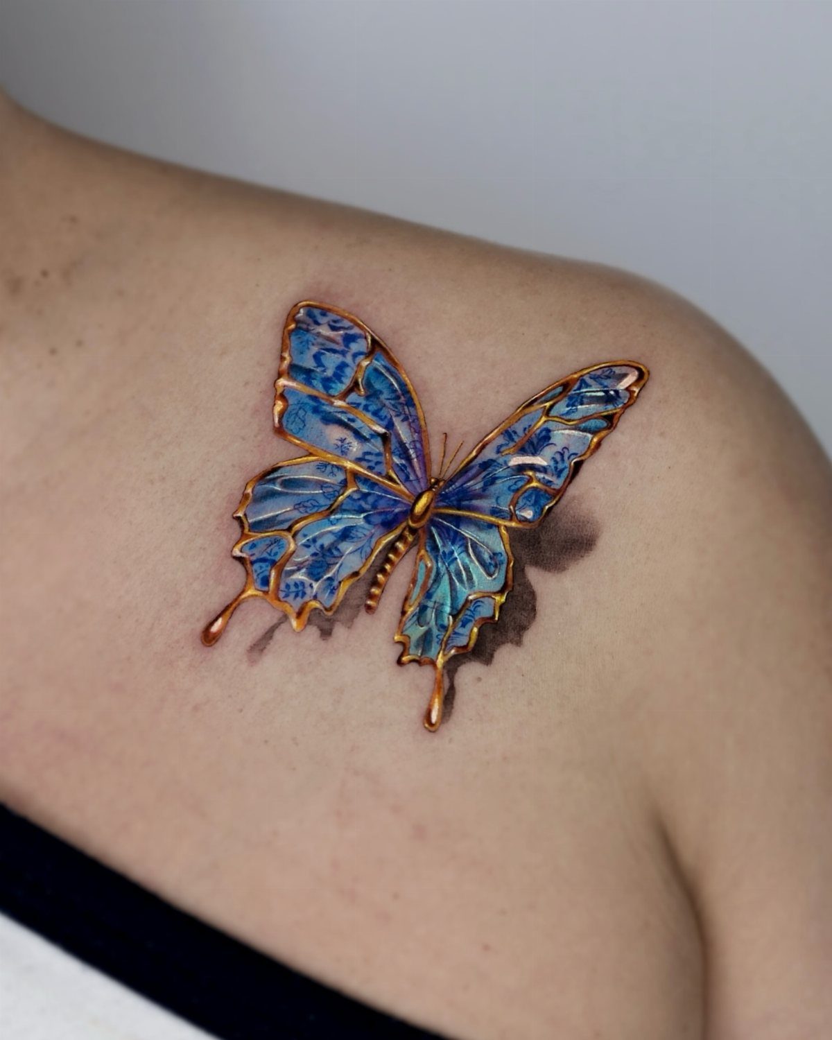Blue and orange butterfly tattoo with 3D shadow on a shoulder
