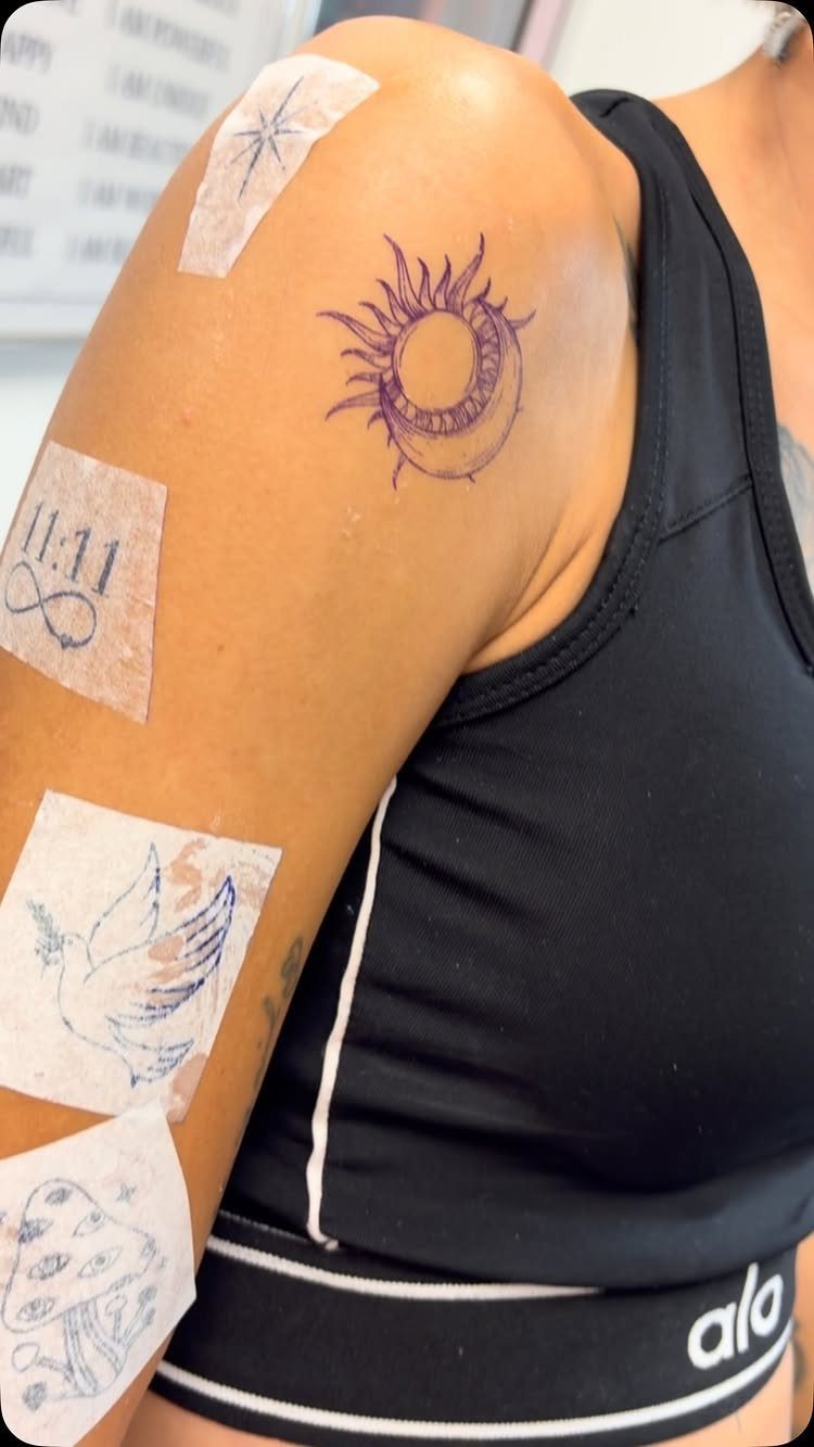 Tattoo stencils of a sun, moon, bird, and mushrooms on a person's arm.