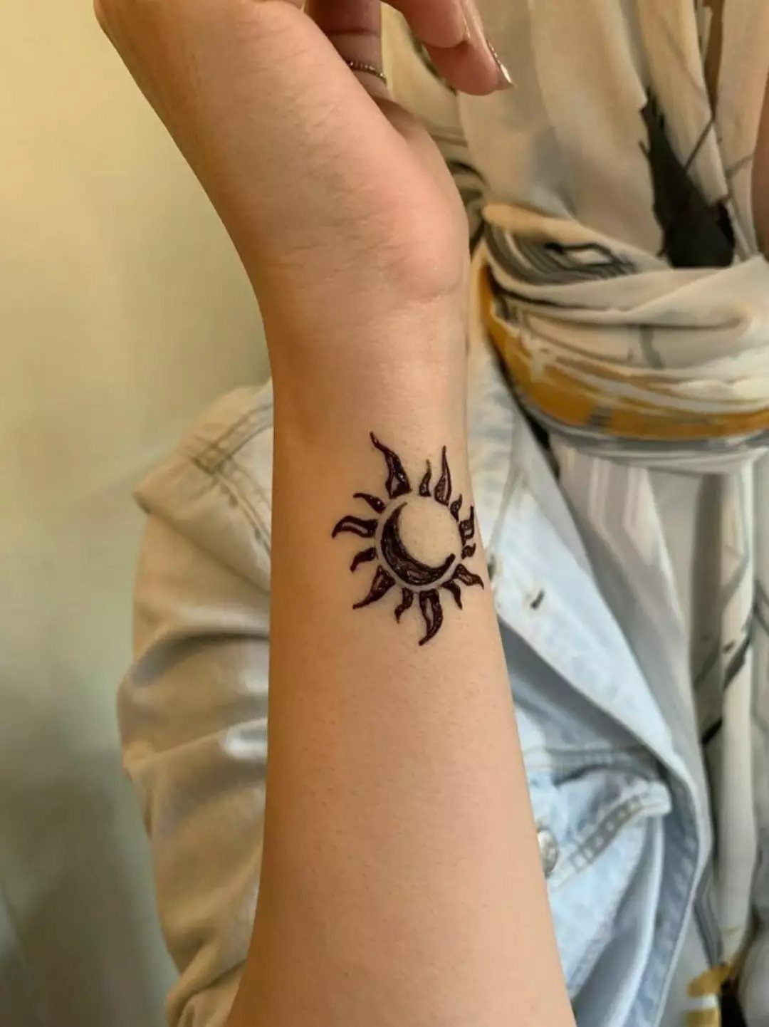 Sun and crescent moon henna tattoo on a person's inner forearm