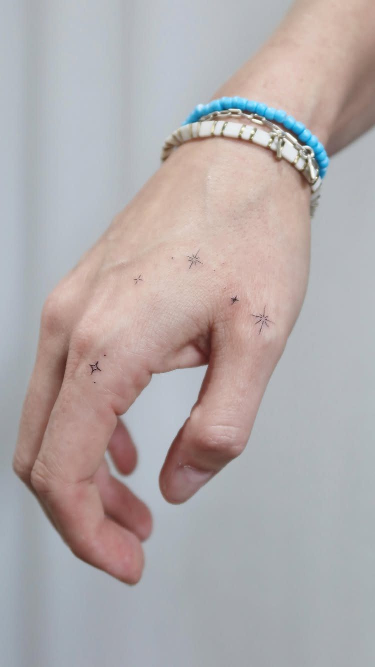 Small black ink fine-line star tattoos on the back of a person's hand.