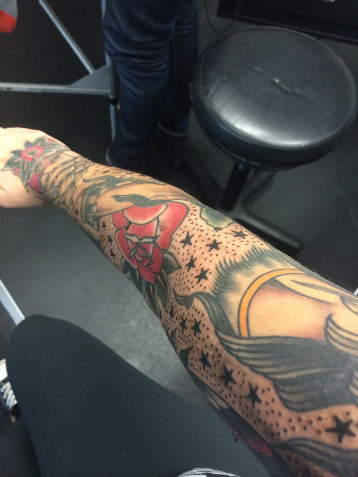 Tattooed arm with red roses and small black five-pointed stars as filler ink.
