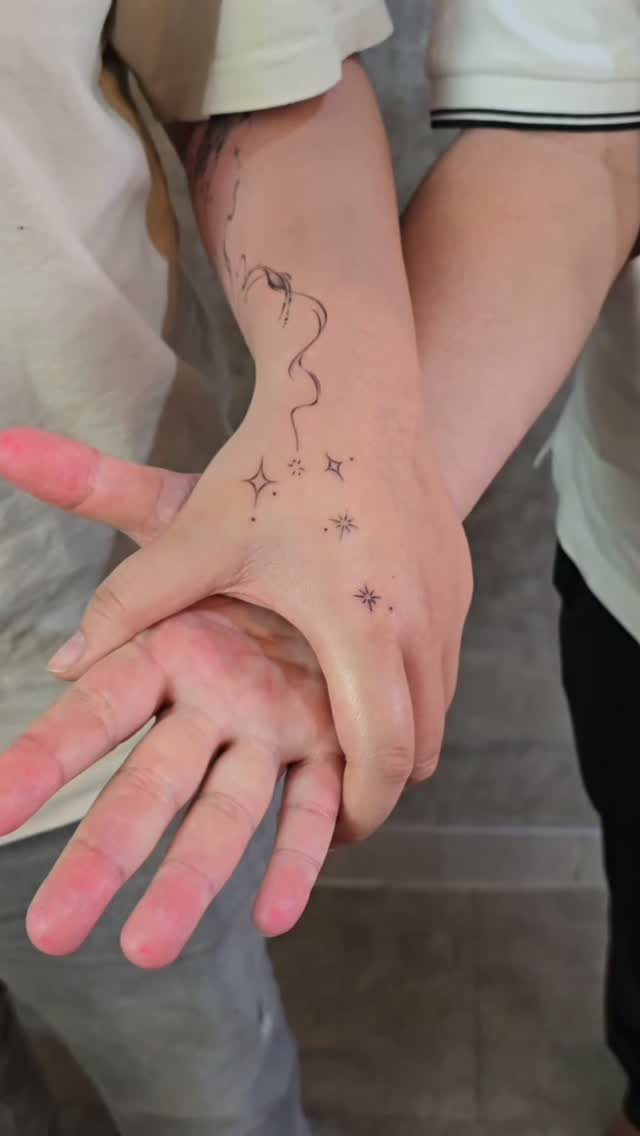 Hand and wrist with small black four-pointed star tattoos and a wavy line.