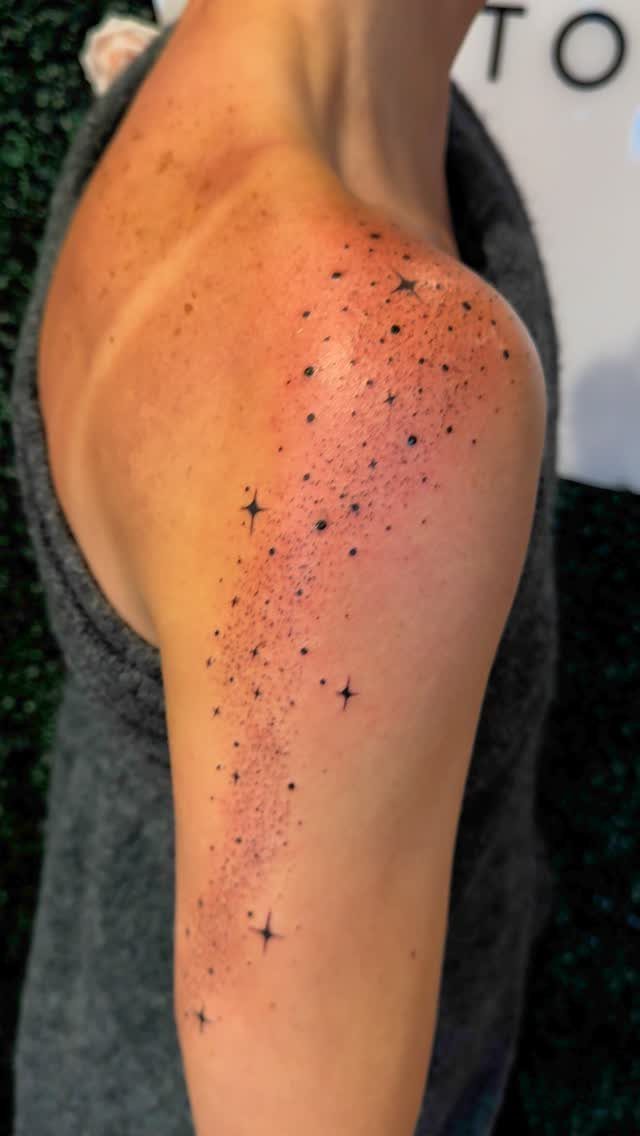 Tattoo of small black four-pointed stars and tiny dots on a person's shoulder