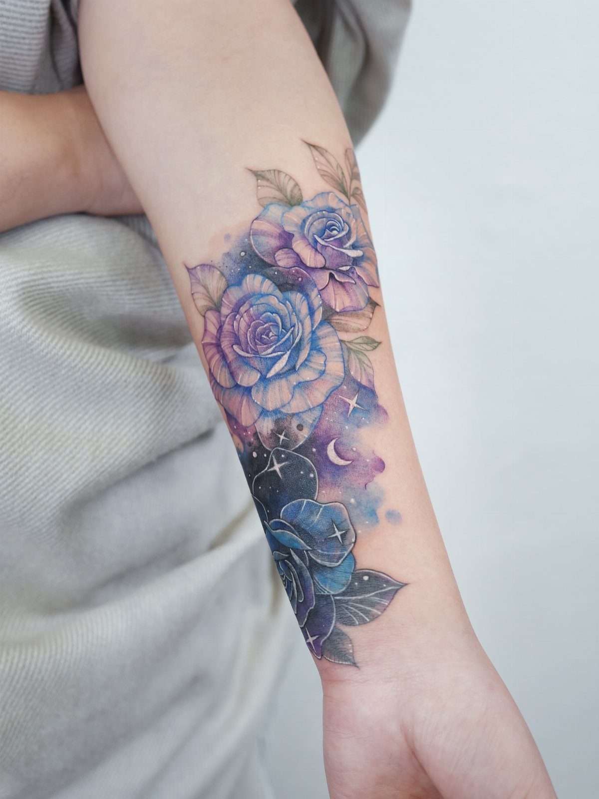Forearm tattoo of purple roses with a crescent moon and small white stars.