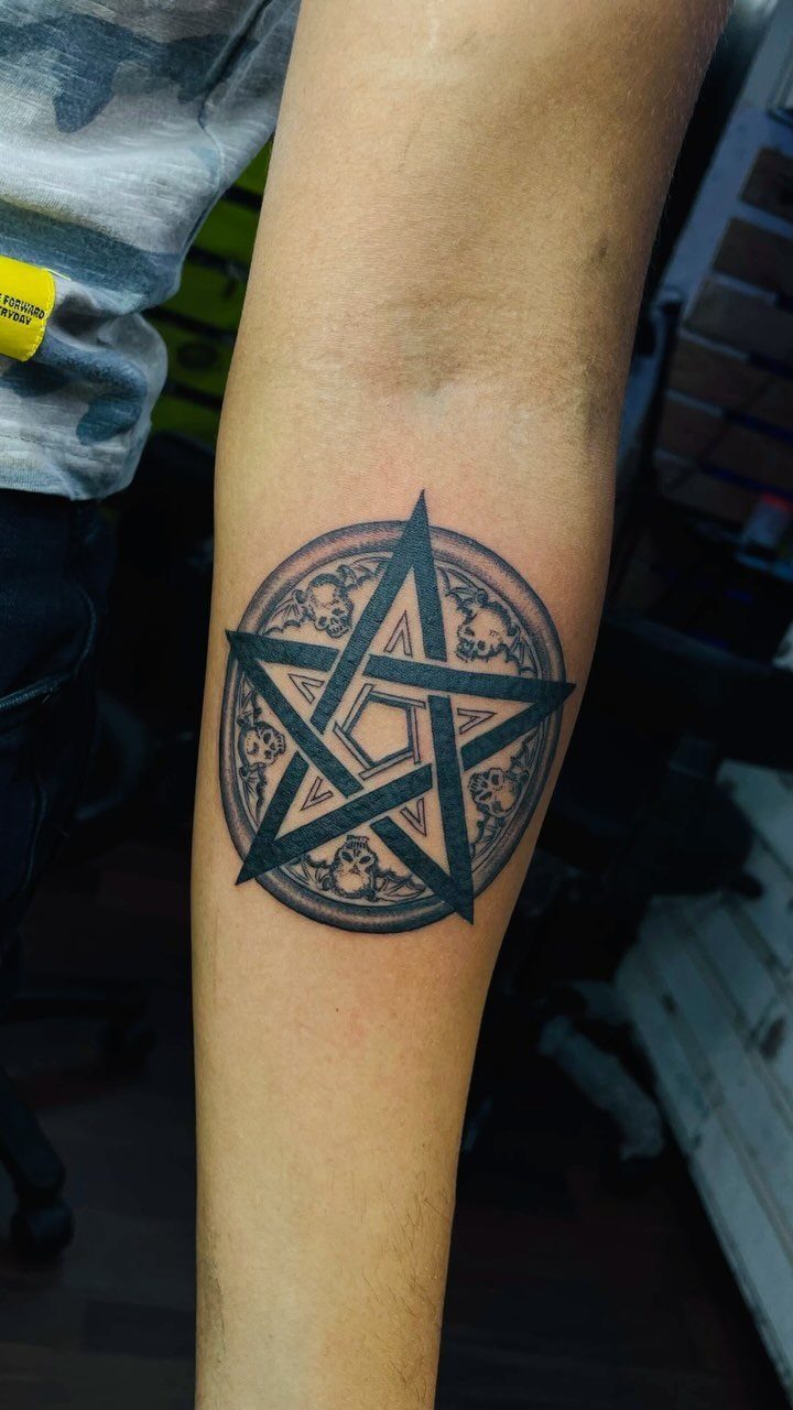 Five-pointed star tattoo with circular ornate detailing on a person's forearm.