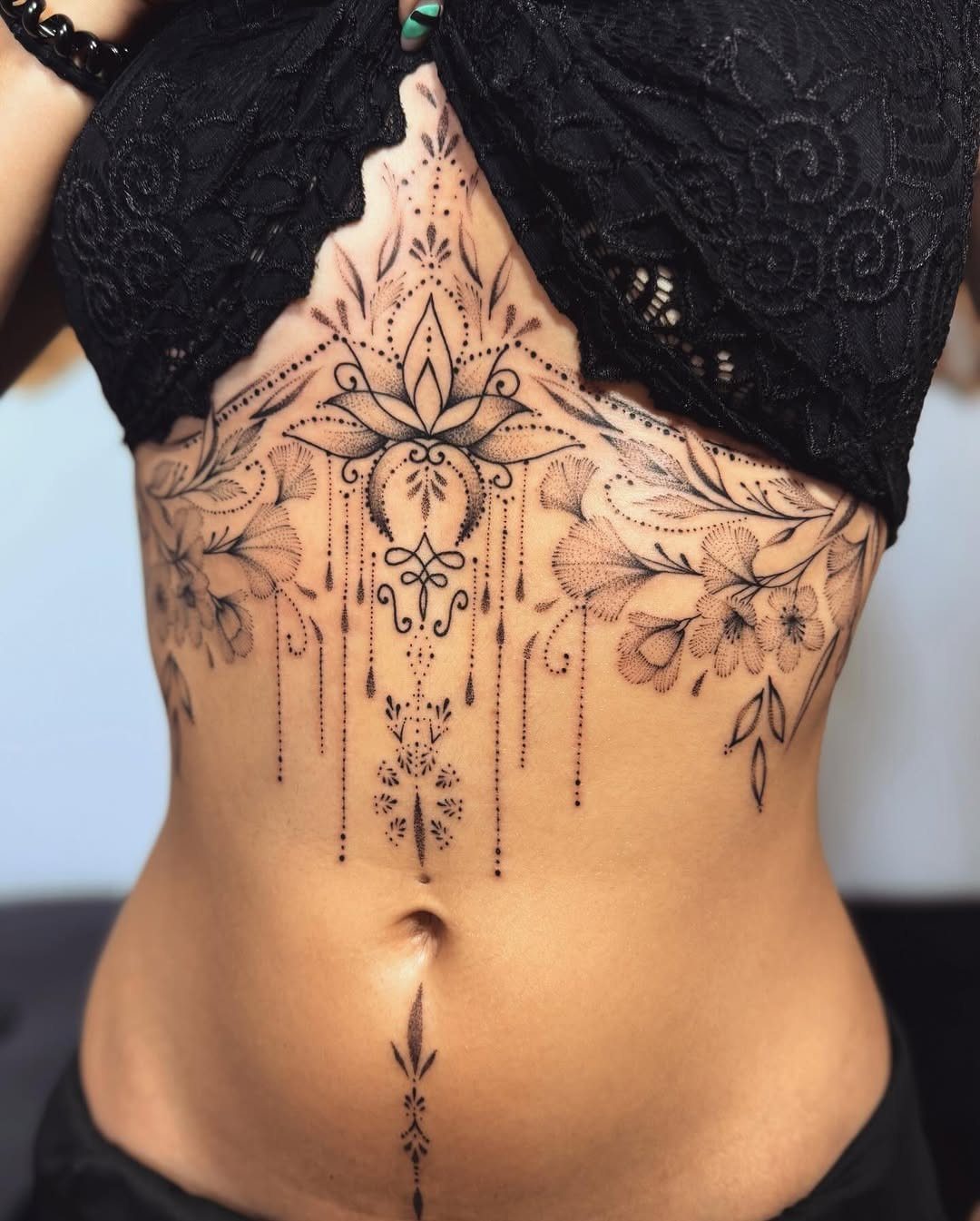 Intricate mandala and floral tattoo covering the upper stomach and rib area
