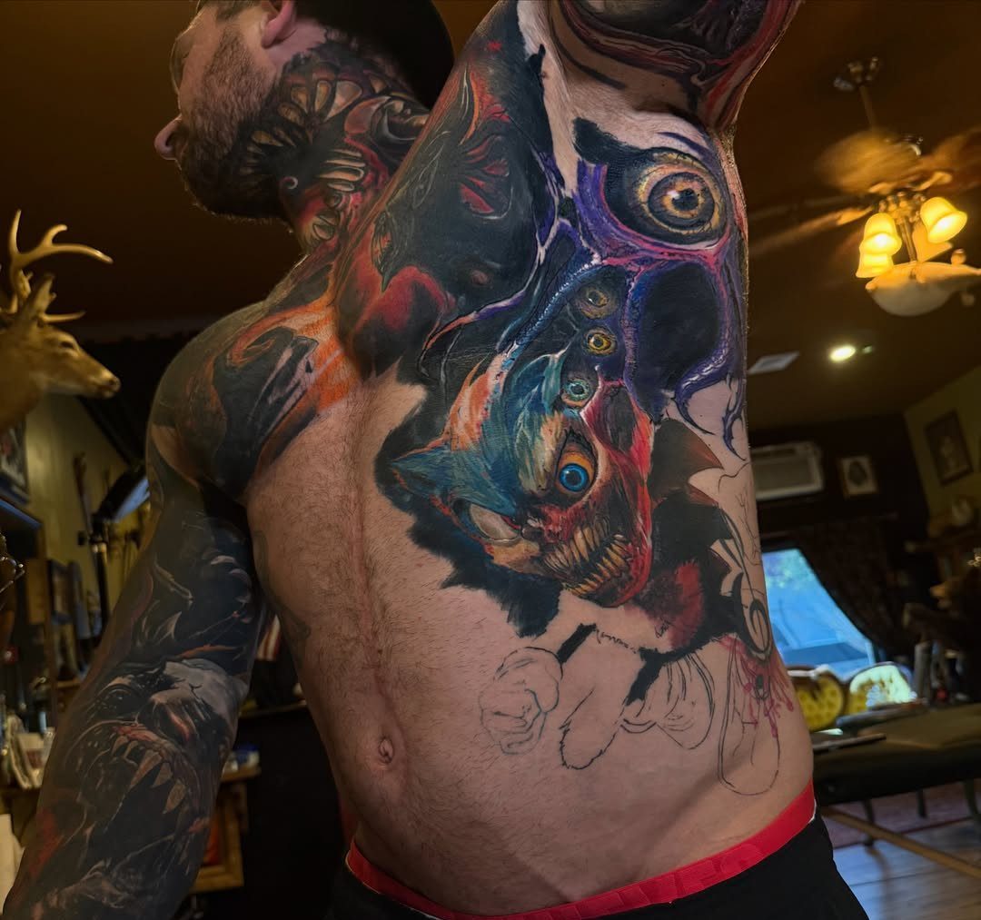 Man's torso with a large, colorful surreal creature tattoo covering his stomach and ribs.