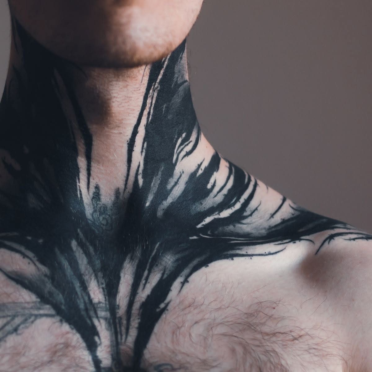 Abstract black ink tattoo with sweeping lines covering a person's neck and chest.