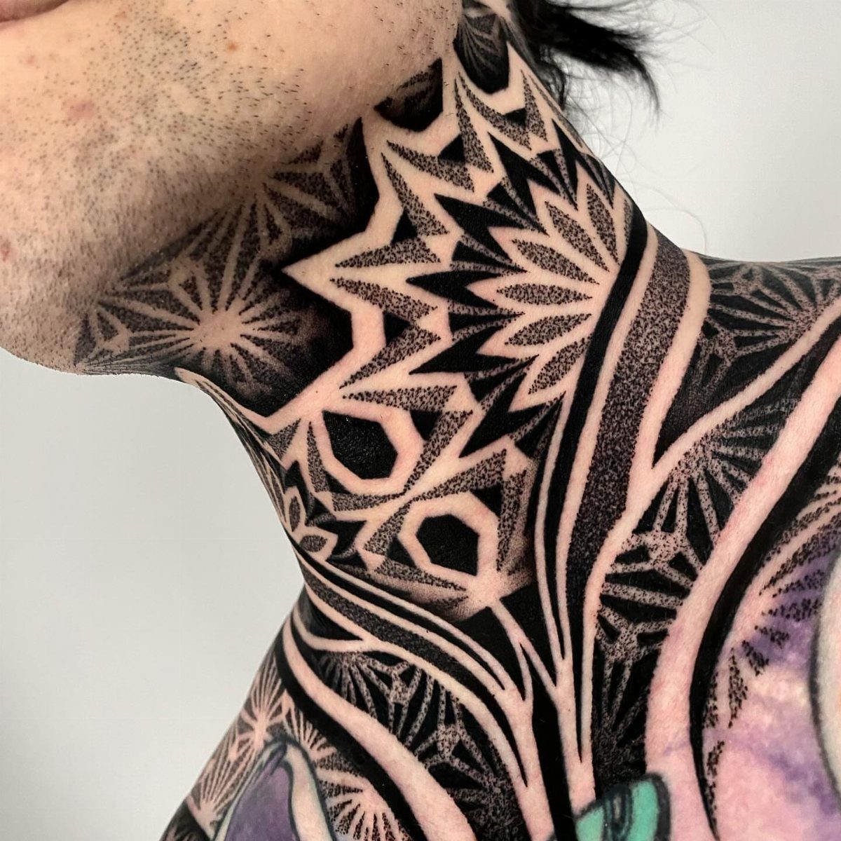Geometric black ink tattoo with symmetrical patterns covering a person's neck.