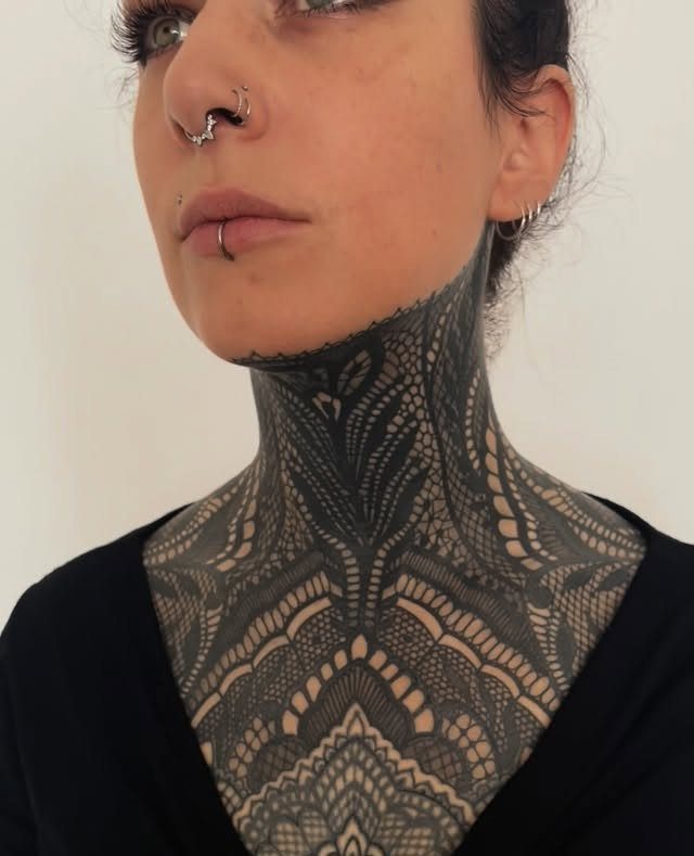 Intricate black ornamental lace tattoo covering the neck and upper chest of a person.