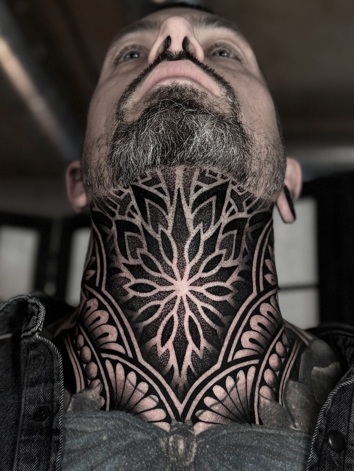 Man's neck with a bold black geometric and ornamental mandala tattoo.