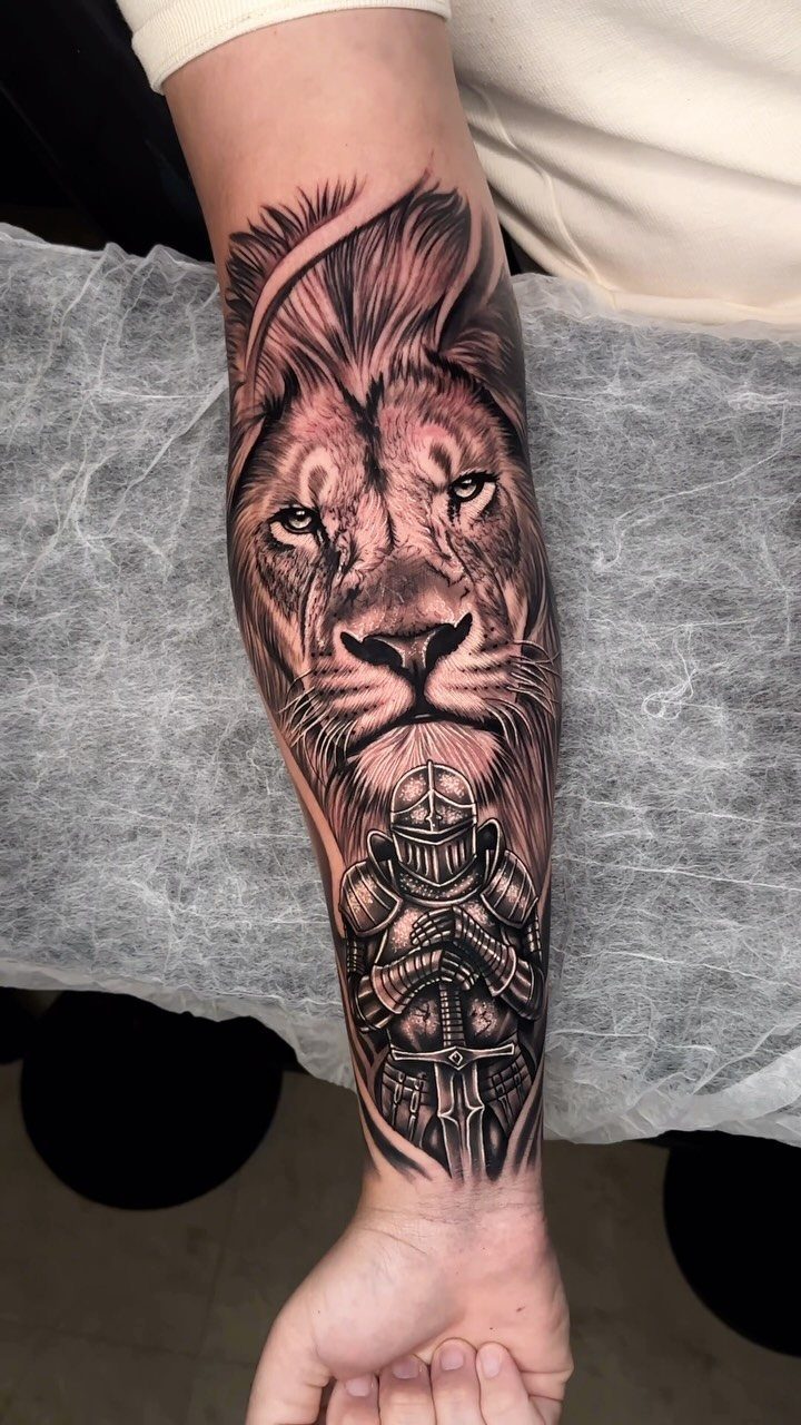 Lion and knight tattoo in black and grey ink on a forearm