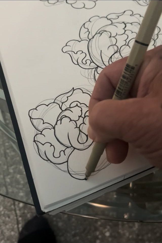 Hand drawing black ink peony flower tattoo designs in a white sketchbook