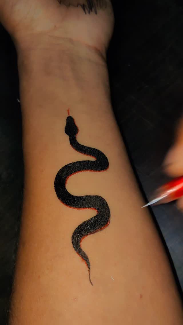 Black snake tattoo with red outline being applied to a person's forearm.