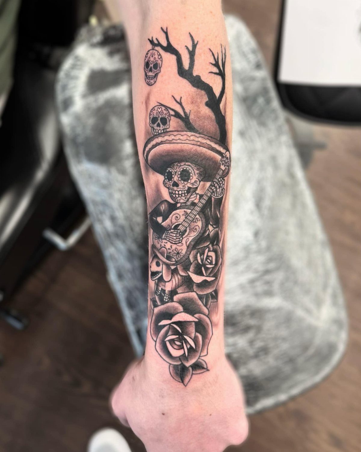 Skeleton in a sombrero playing guitar with roses tattoo on a forearm