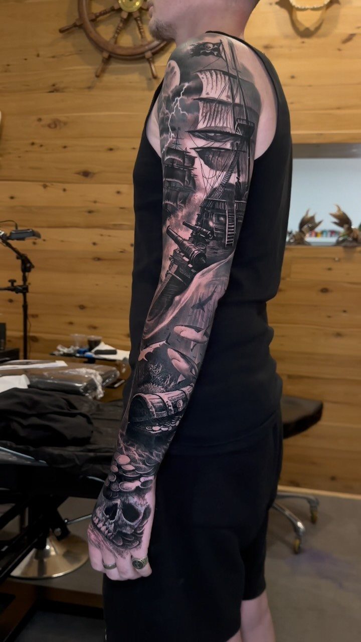 Sleeve tattoo featuring a detailed sailing ship and a skull on the hand