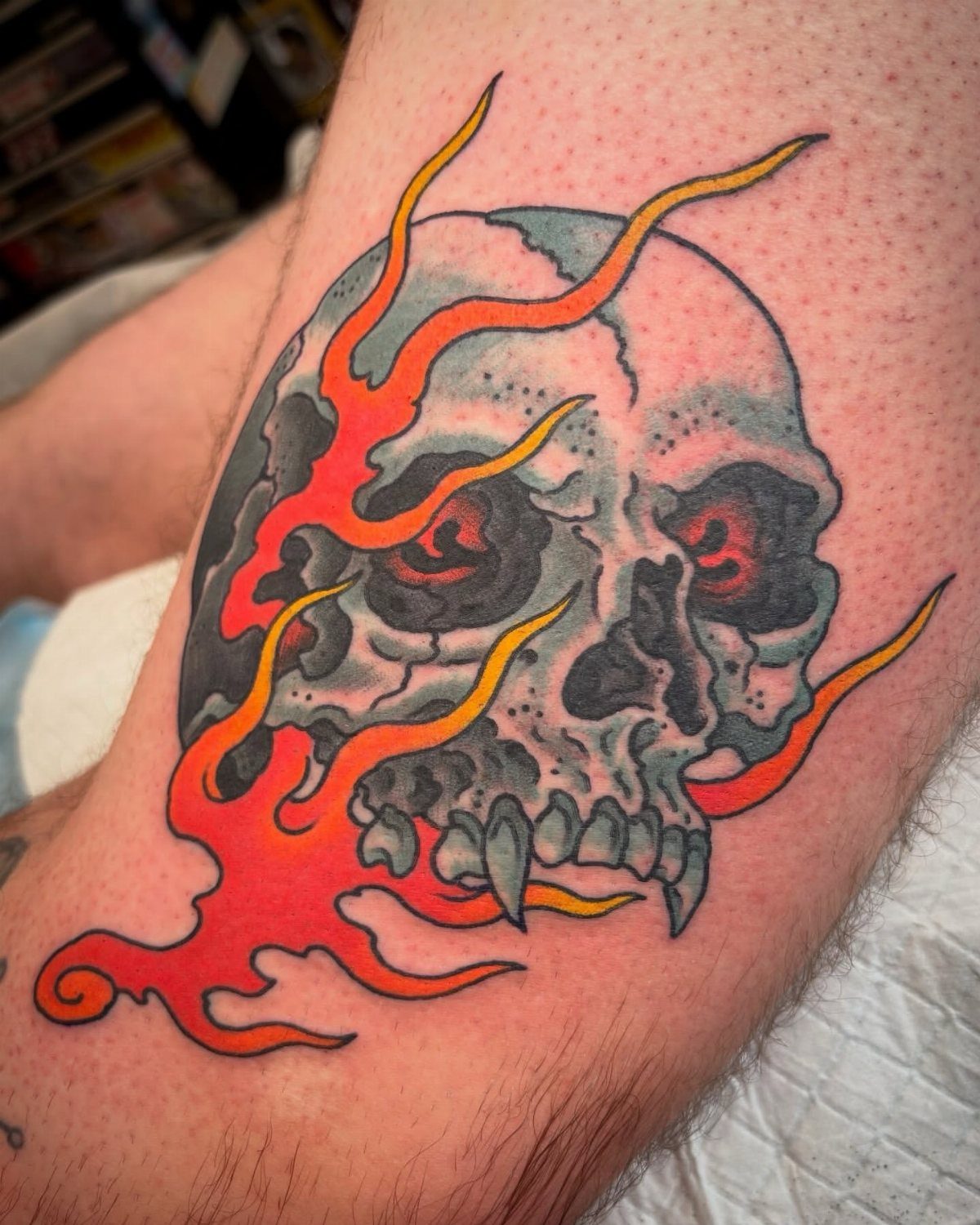 Skull tattoo with red eyes surrounded by bright orange and red flames on skin