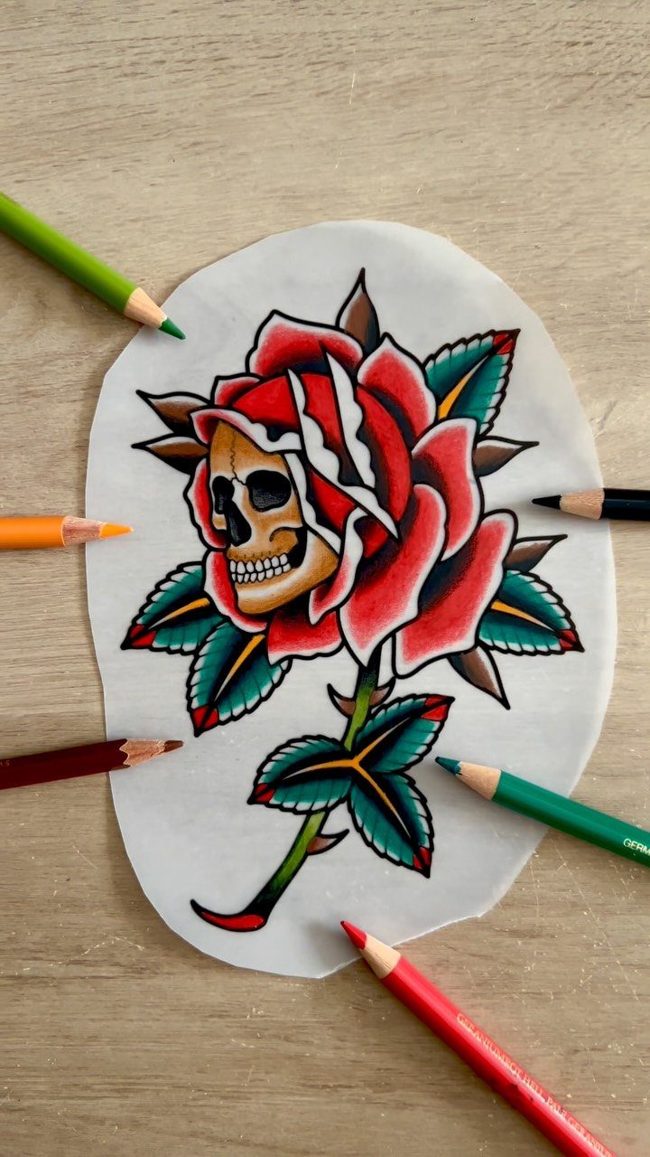 Skull integrated with a red rose drawing surrounded by colored pencils on wood.