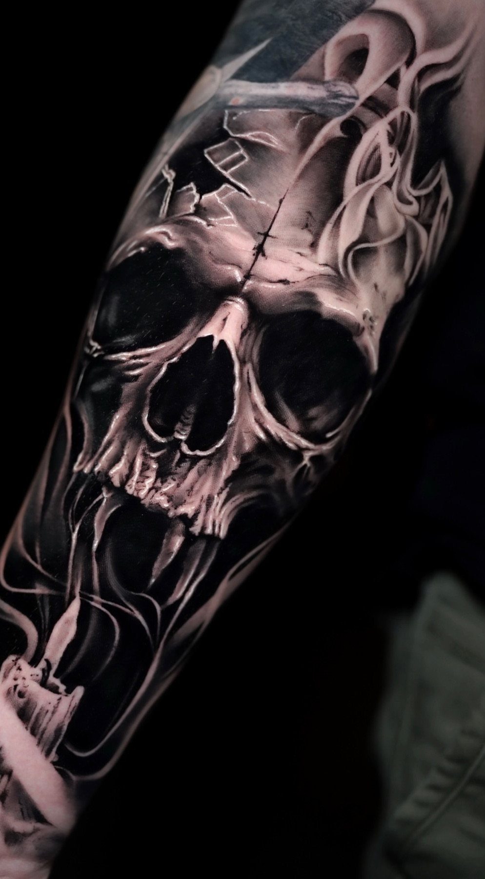 Detailed black and grey skull tattoo surrounded by swirling smoke on an arm.