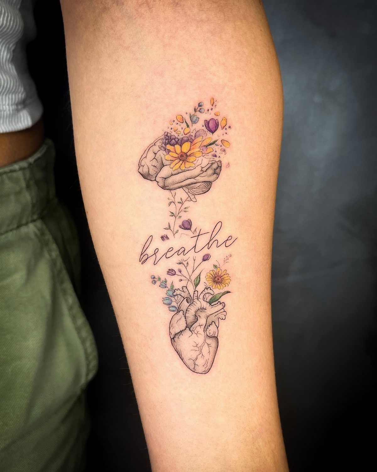 Tattoo on an arm showing a brain and heart with colorful flowers.