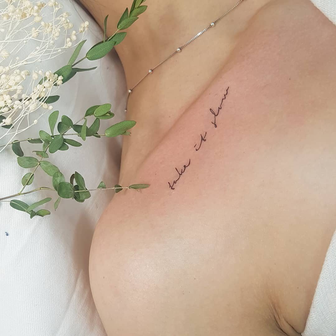 Cursive black ink tattoo reading take it slow on a person's collarbone area