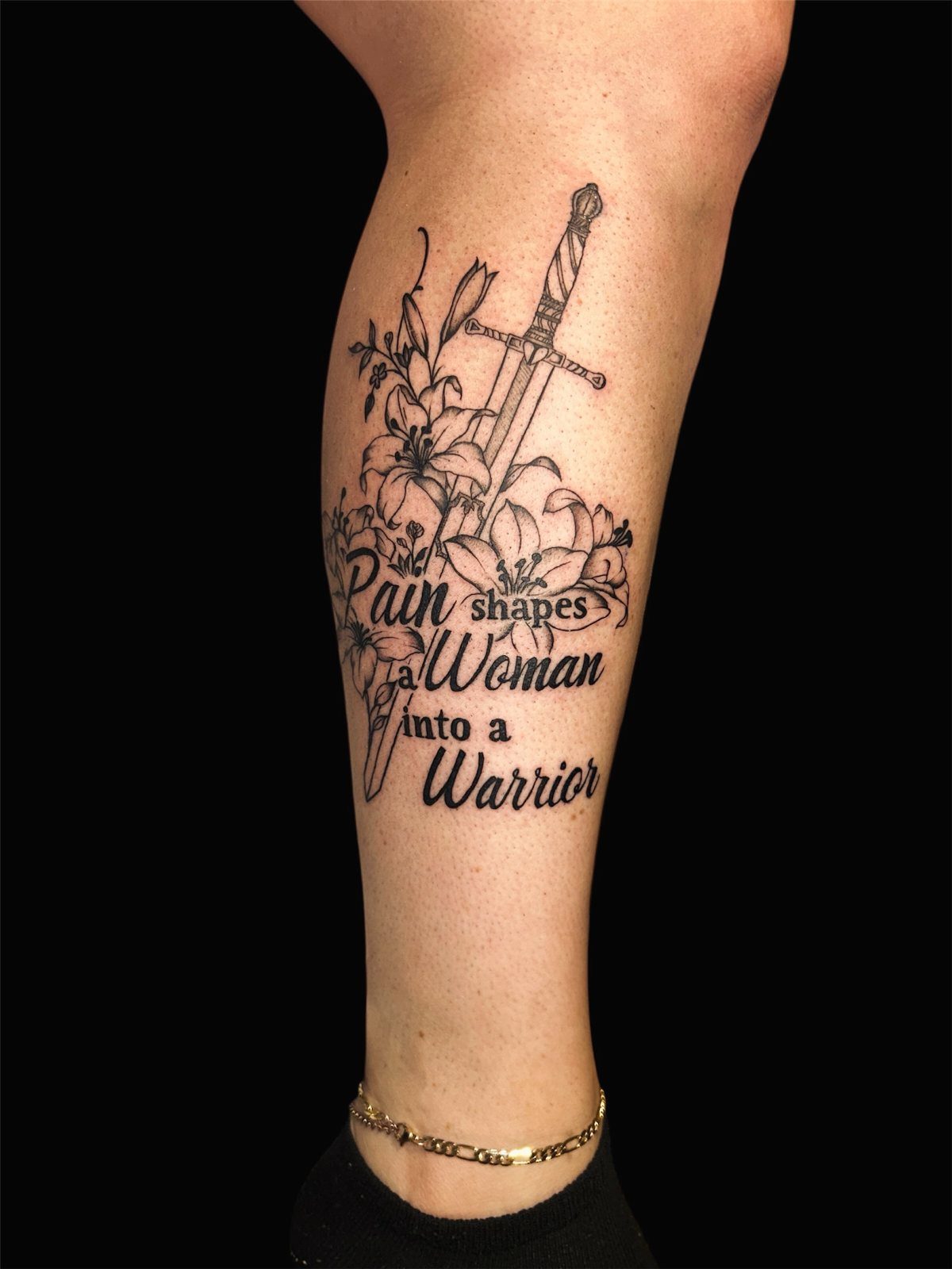 Warrior tattoo on a leg with a sword, lilies, and inspirational text.