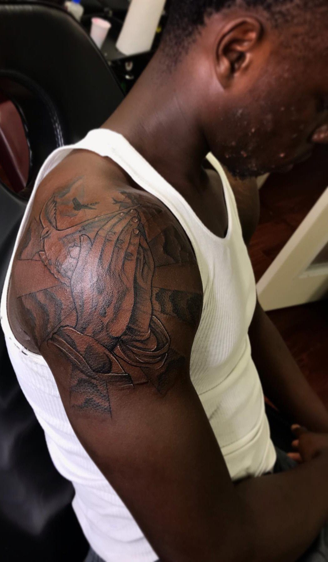 Praying hands tattoo in black and grey ink on a dark-skinned arm.