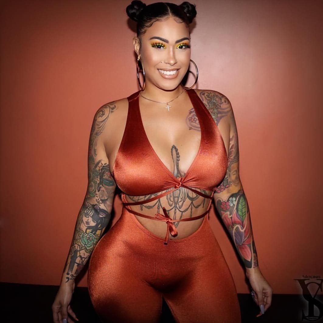 Woman with dark skin showing colorful and black ink tattoos on her arms and torso.